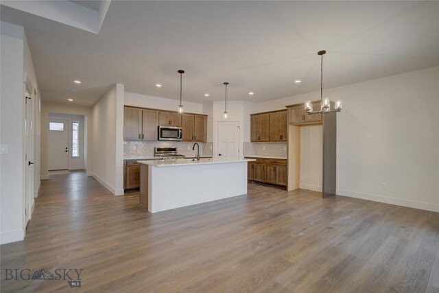 kitchen with a center island with sink, hanging light fixtures, light wood-type flooring, and appliances with stainless steel finishes