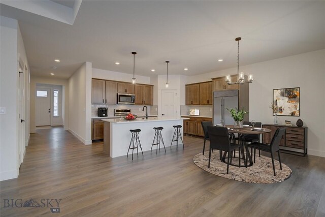 kitchen featuring hardwood / wood-style flooring, hanging light fixtures, appliances with stainless steel finishes, and an island with sink