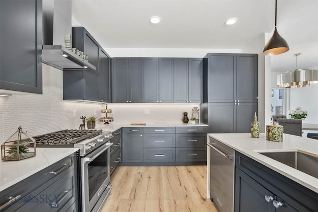 kitchen with light wood-type flooring, wall chimney exhaust hood, gray cabinetry, stainless steel appliances, and hanging light fixtures