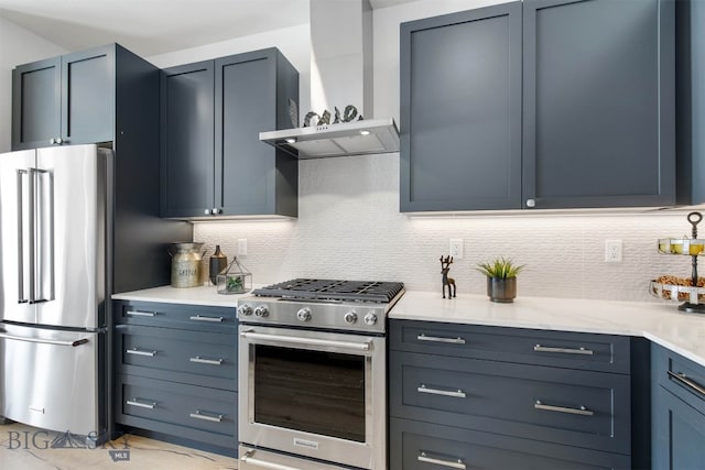 kitchen with blue cabinetry, light stone countertops, stainless steel appliances, wall chimney range hood, and tasteful backsplash