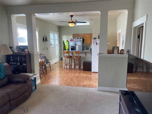 living room featuring ceiling fan, light hardwood / wood-style floors, ornamental molding, and decorative columns