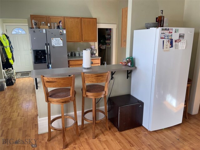 kitchen with stainless steel fridge with ice dispenser, light hardwood / wood-style flooring, kitchen peninsula, white fridge, and a breakfast bar