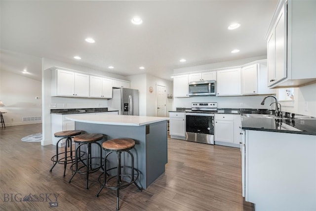 kitchen featuring a kitchen breakfast bar, dark hardwood / wood-style flooring, stainless steel appliances, a center island, and white cabinetry