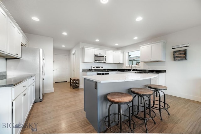 kitchen with a center island, light wood-type flooring, a kitchen bar, white cabinetry, and stainless steel appliances