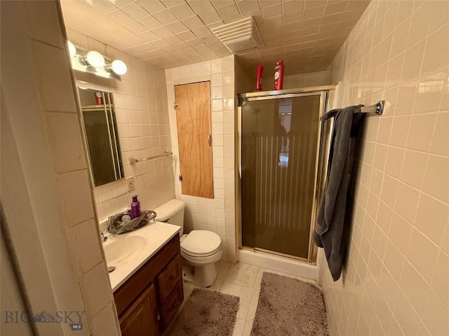 bathroom with tile patterned floors, vanity, a shower with door, tile walls, and toilet