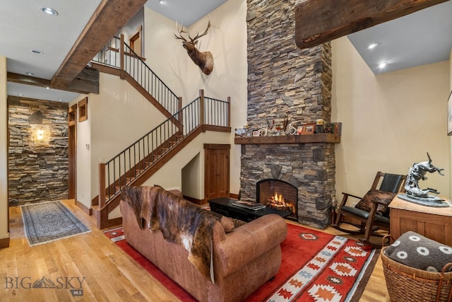 living room with beamed ceiling, a high ceiling, light hardwood / wood-style flooring, and a stone fireplace