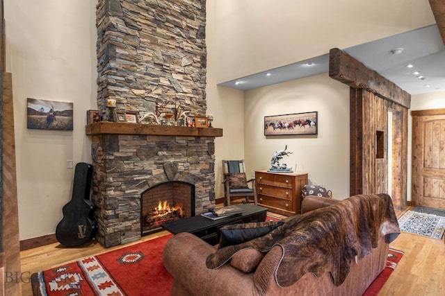 living room with hardwood / wood-style floors, a towering ceiling, and a stone fireplace