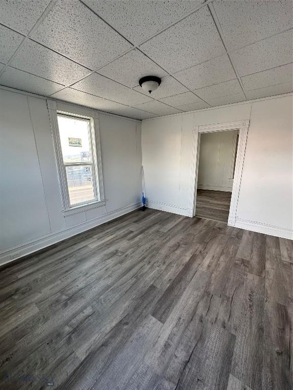 spare room with a drop ceiling and dark wood-type flooring