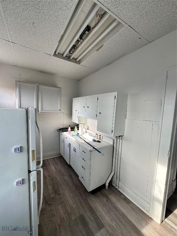 kitchen with a paneled ceiling, white refrigerator, white cabinetry, and dark wood-type flooring