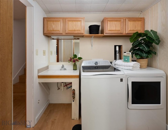 clothes washing area featuring cabinets, light hardwood / wood-style floors, and washer and clothes dryer