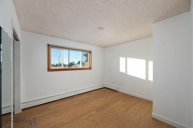 empty room with wood-type flooring, a textured ceiling, and a baseboard radiator