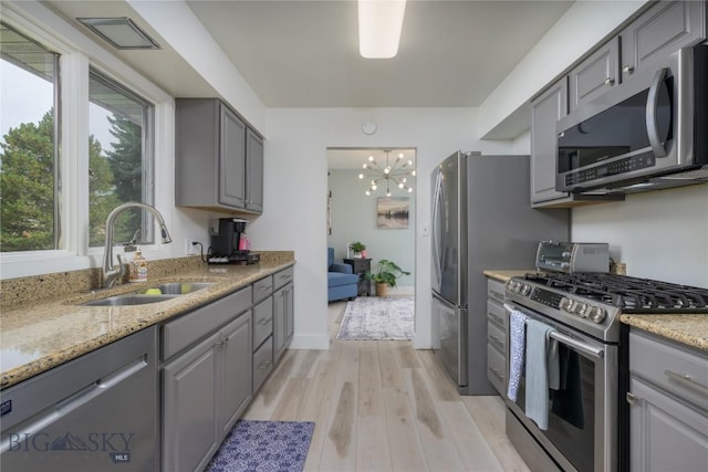 kitchen featuring appliances with stainless steel finishes, light wood-type flooring, sink, a notable chandelier, and gray cabinets