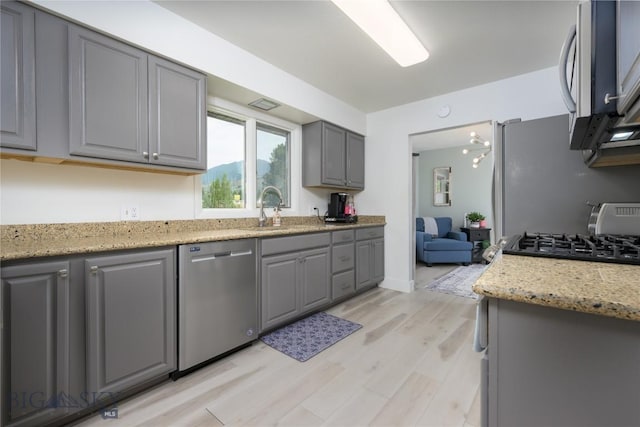 kitchen featuring light stone countertops, appliances with stainless steel finishes, light wood-type flooring, sink, and gray cabinets