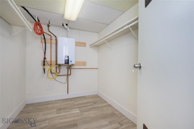 walk in closet featuring water heater, light hardwood / wood-style flooring, and a drop ceiling