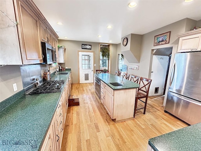 kitchen with sink, stainless steel appliances, light hardwood / wood-style floors, a breakfast bar area, and a kitchen island