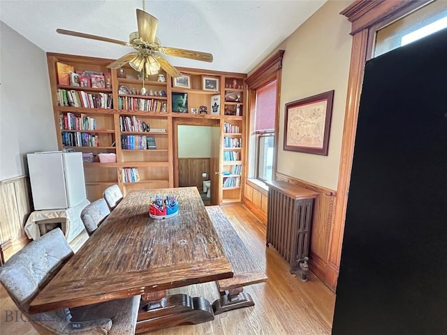 home office featuring built in shelves, light hardwood / wood-style floors, radiator, and ceiling fan