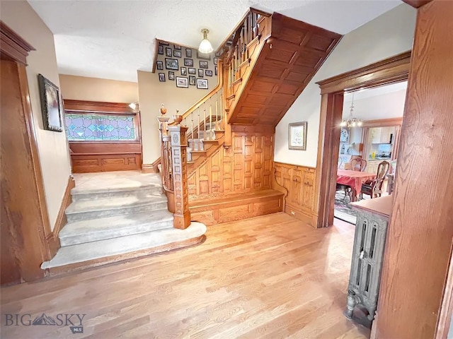 staircase featuring wooden walls, wood-type flooring, and a notable chandelier