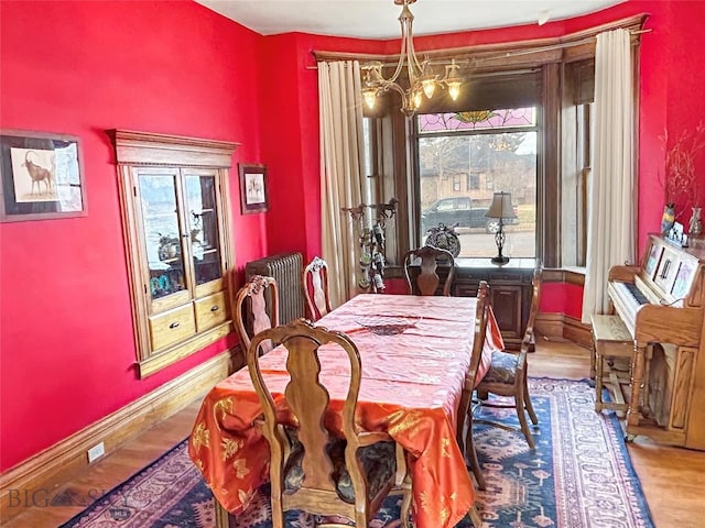 dining space featuring radiator, wood-type flooring, and a notable chandelier