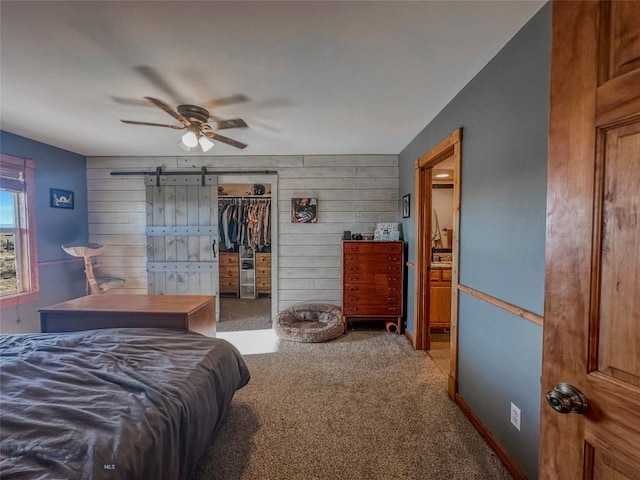 carpeted bedroom featuring a walk in closet, ceiling fan, wooden walls, a barn door, and a closet