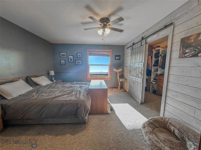 carpeted bedroom with a walk in closet, a barn door, a closet, and ceiling fan