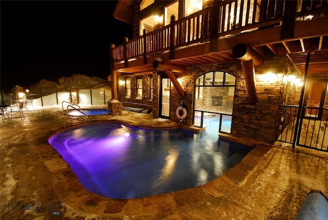 pool at night with a patio and a hot tub