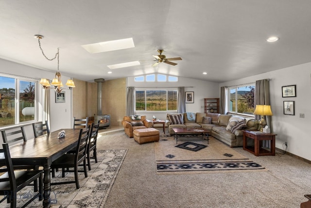 carpeted living room with ceiling fan with notable chandelier, a wood stove, and lofted ceiling with skylight