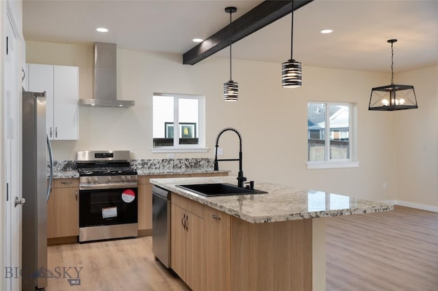 kitchen with light wood-style flooring, light stone countertops, stainless steel appliances, wall chimney range hood, and a sink