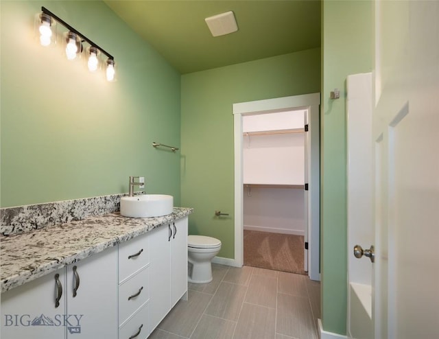 bathroom with a washtub, toilet, vanity, baseboards, and a spacious closet