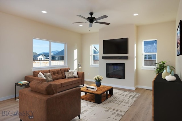 living room featuring ceiling fan, recessed lighting, baseboards, light wood finished floors, and a glass covered fireplace