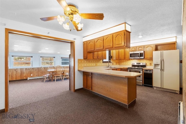 kitchen with appliances with stainless steel finishes, dark colored carpet, light countertops, and a peninsula