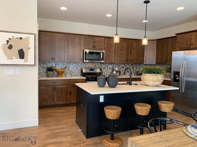 kitchen with hanging light fixtures, stainless steel appliances, a kitchen breakfast bar, a center island with sink, and light wood-type flooring