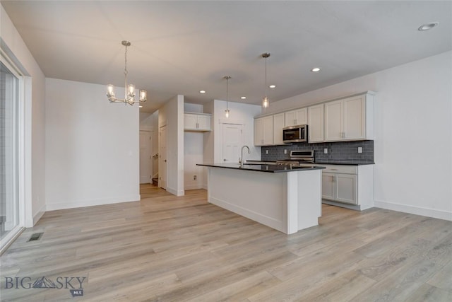 kitchen featuring a center island with sink, stainless steel appliances, pendant lighting, and white cabinetry