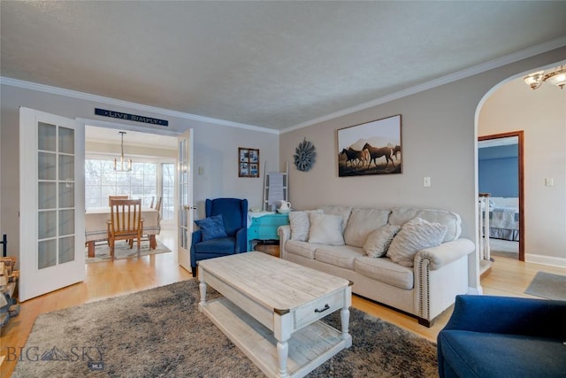 living room featuring french doors, light hardwood / wood-style floors, ornamental molding, and a notable chandelier