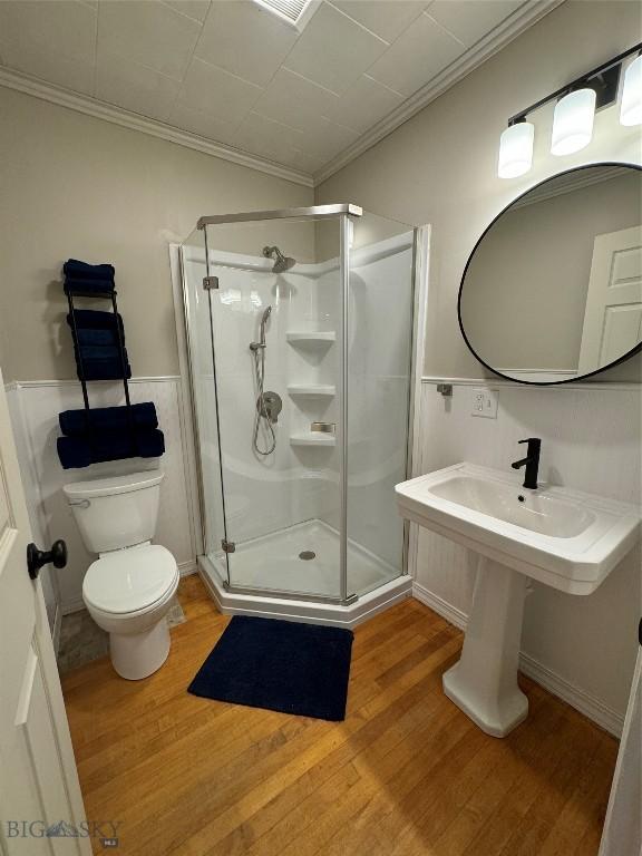 bathroom with crown molding, hardwood / wood-style floors, an enclosed shower, and toilet