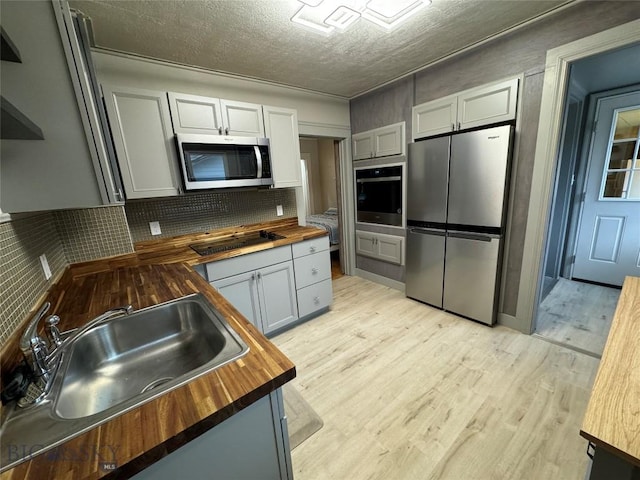 kitchen featuring wooden counters, appliances with stainless steel finishes, a textured ceiling, sink, and light hardwood / wood-style flooring