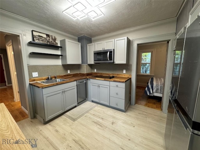 kitchen with decorative backsplash, appliances with stainless steel finishes, light hardwood / wood-style floors, gray cabinets, and butcher block counters