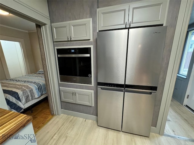 kitchen with appliances with stainless steel finishes, light wood-type flooring, and ornamental molding