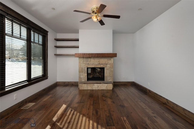 unfurnished living room featuring a stone fireplace, a wealth of natural light, and dark wood-type flooring