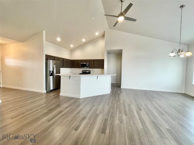 kitchen featuring high vaulted ceiling, hanging light fixtures, light wood-type flooring, appliances with stainless steel finishes, and dark brown cabinetry