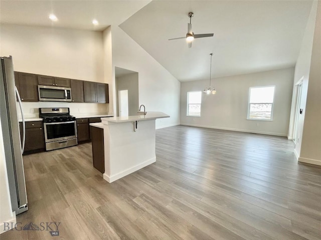 kitchen with light wood-type flooring, dark brown cabinetry, stainless steel appliances, a kitchen island with sink, and high vaulted ceiling