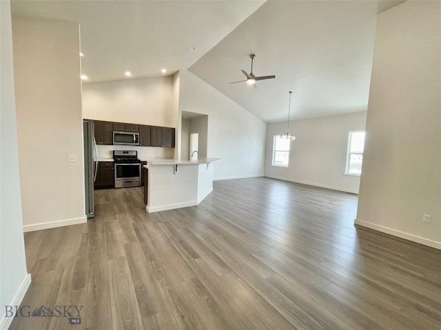 unfurnished living room featuring high vaulted ceiling, ceiling fan with notable chandelier, and light wood-type flooring