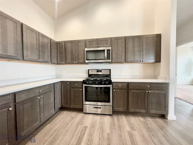 kitchen featuring dark brown cabinets, a towering ceiling, stainless steel appliances, and light wood-type flooring