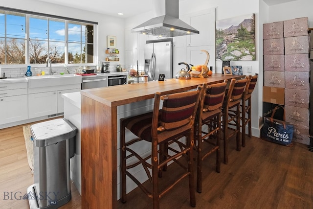 kitchen with appliances with stainless steel finishes, hardwood / wood-style flooring, butcher block countertops, white cabinetry, and range hood