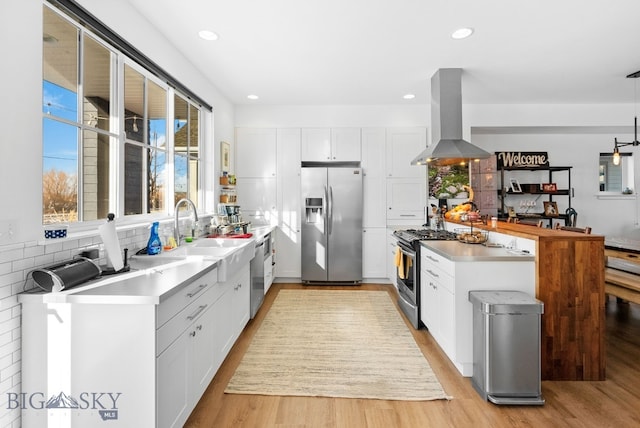 kitchen featuring island exhaust hood, appliances with stainless steel finishes, decorative light fixtures, white cabinets, and light wood-type flooring