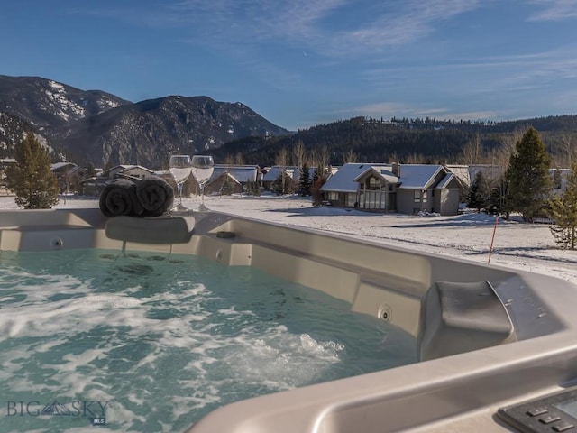 snow covered pool with a mountain view and a hot tub