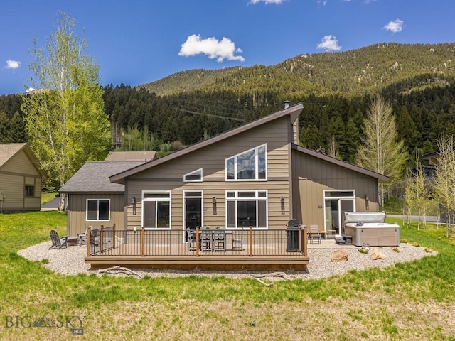 1880 Little Coyote, Big Sky, MT 59716 - back of property with a hot tub, a deck with mountain view, a wooded view, a yard, and board and batten siding