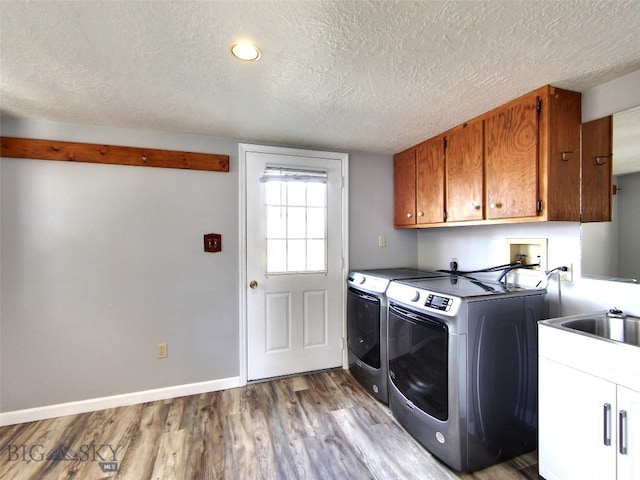 laundry area with washing machine and clothes dryer, sink, cabinets, a textured ceiling, and light wood-type flooring