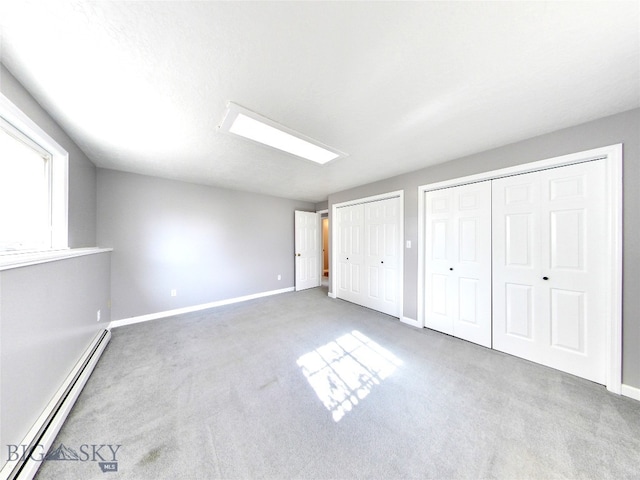 unfurnished bedroom featuring a textured ceiling, carpet, a baseboard radiator, and two closets