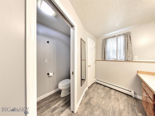 bathroom with a baseboard heating unit, a textured ceiling, toilet, vanity, and hardwood / wood-style flooring