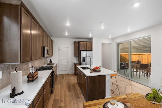 kitchen with sink, stainless steel appliances, tasteful backsplash, light hardwood / wood-style flooring, and an island with sink